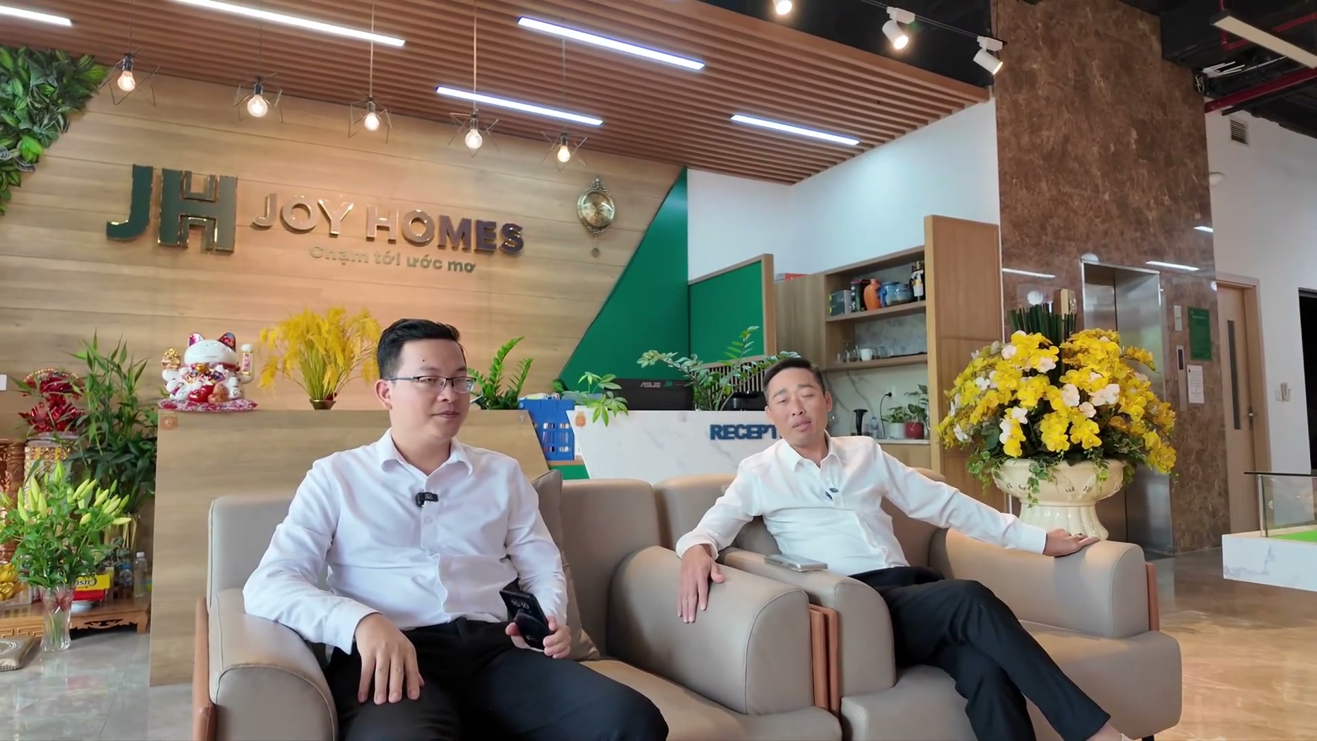 Hai người ngồi trò chuyện tại quầy tiếp khách văn phòng trong Ecopark trước khi đi Alluvia City