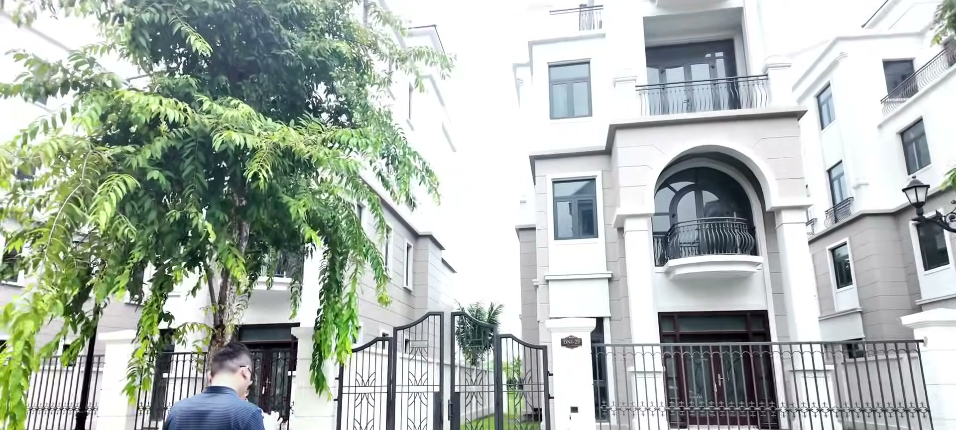 Ban công sắt uốn và ô cửa vòm của một căn đơn lập trong phân khu Đảo Ngọc, tán cây rủ trước mặt tiền