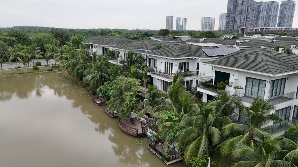 Dãy biệt thự đảo Ecopark nhìn từ trên cao, phía sau mỗi căn là một khoảng decking gỗ có lan can nhô ra sát mép nước, xen giữa là hàng dừa