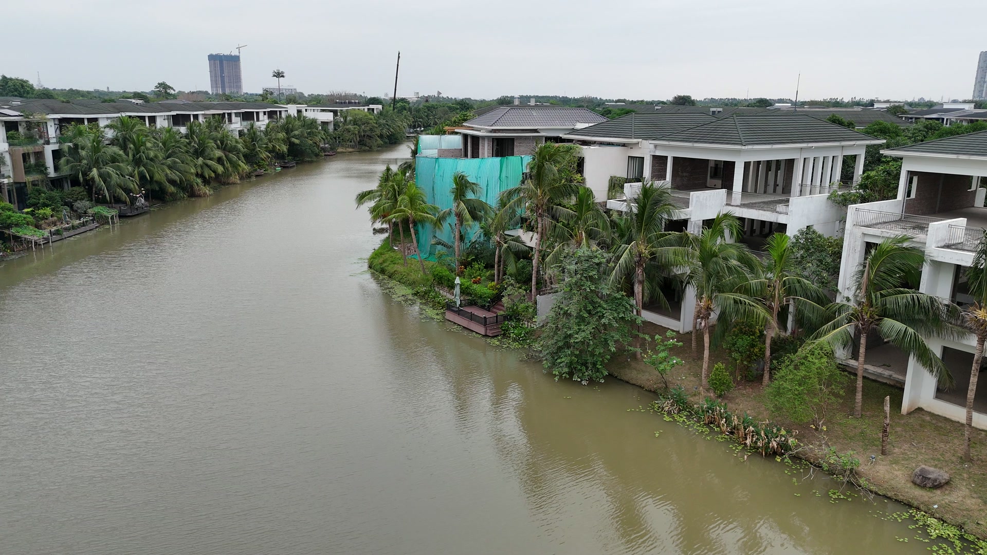 Dòng sông rộng chạy giữa hai dãy biệt thự đảo Ecopark, một bên là các căn đã ở với hàng dừa và sàn decking sát nước, một bên là những căn còn đang xây thô