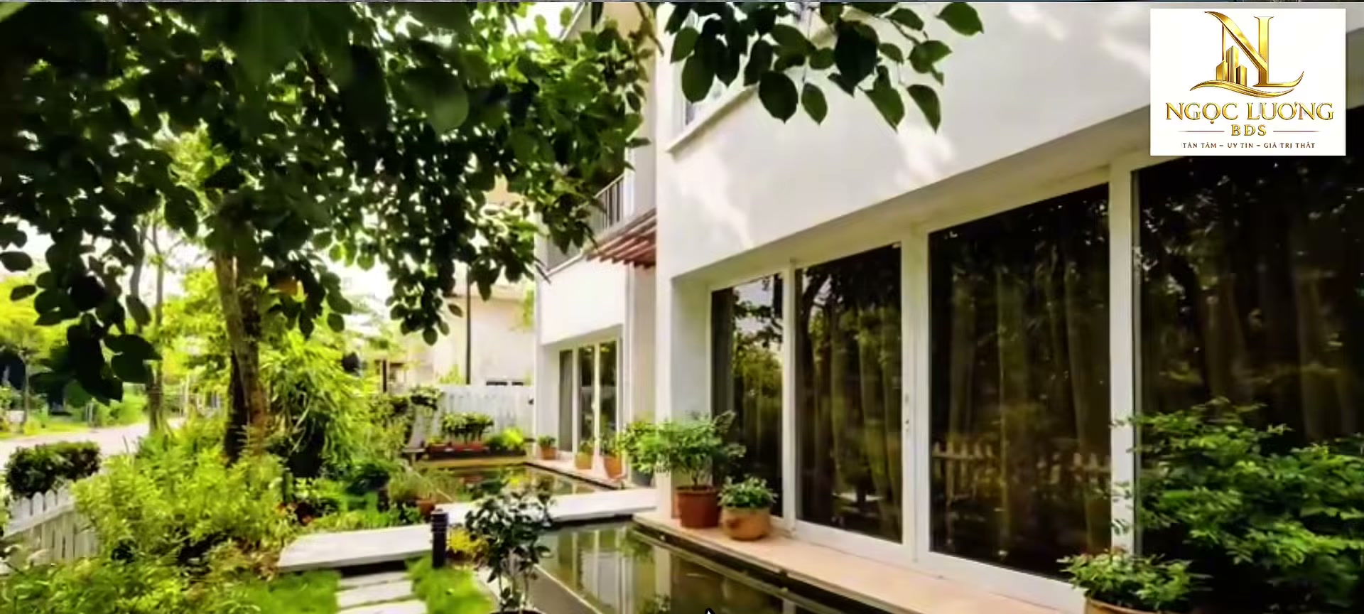 Biệt thự trong Ecopark với bể nước chạy dọc mặt kính, lối đi lát đá và tán cây lớn đã trưởng thành phủ bóng quanh nhà