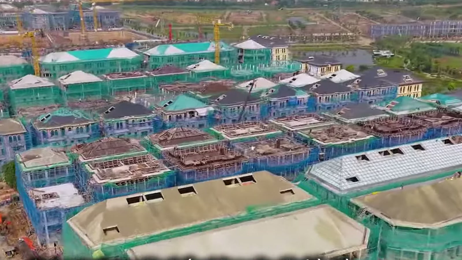 Nhìn từ trên cao xuống dãy nhà thấp tầng Alluvia City đã lợp mái, giàn giáo và lưới xanh còn quây quanh, cần cẩu đứng xen giữa các dãy