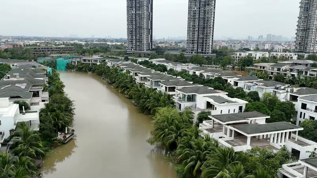 Biệt thự đảo Ecopark nhìn từ trên cao, hai dãy nhà mái sẫm nằm hai bên nhánh nước, phía sau là các toà cao tầng Ecopark