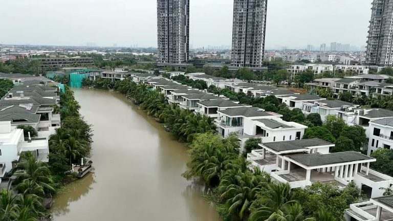 Biệt thự đảo Ecopark nhìn từ trên cao, hai dãy nhà mái sẫm nằm hai bên nhánh nước, phía sau là các toà cao tầng Ecopark