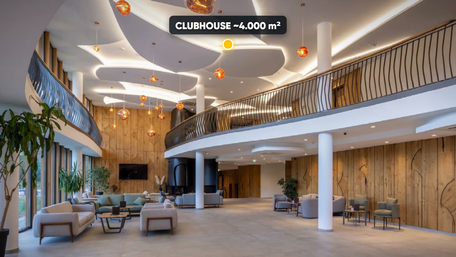 Sảnh clubhouse của khu onsen villa Alluvia City với trần uốn lượn, đèn thả màu cam, sofa và lan can gỗ trên tầng lửng