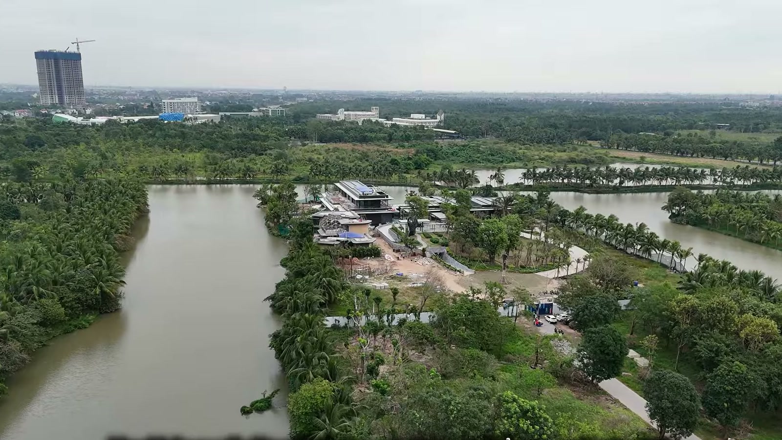 Nhìn từ trên cao xuống một nhánh sông trong khu biệt thự đảo Ecopark, khu nhà câu lạc bộ đang hoàn thiện nằm giữa hàng dừa, phía xa là toà nhà cao tầng đang xây