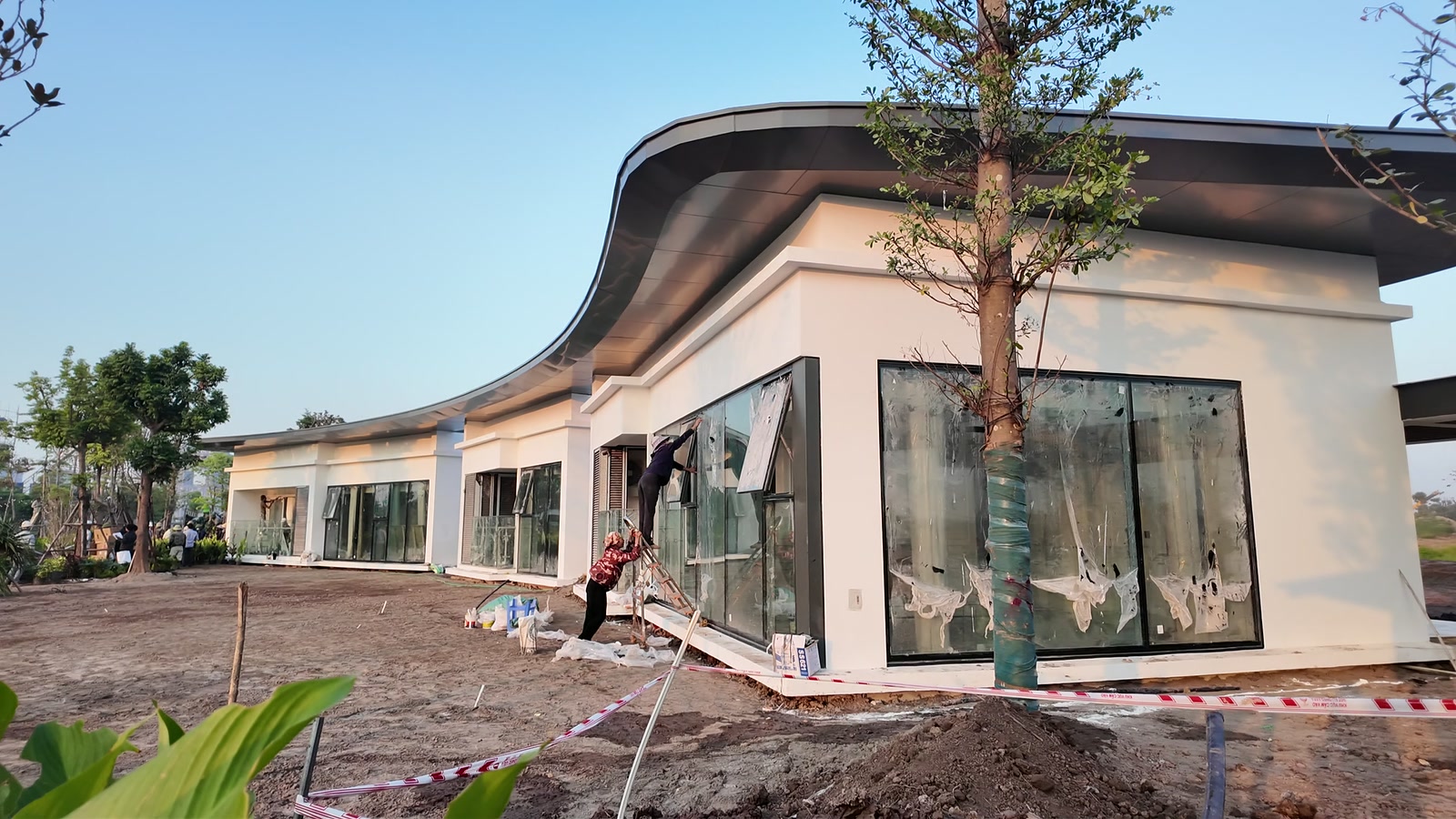 Công nhân bóc lớp kính bảo vệ tại nhà mẫu cao tầng Alumi, phía sau là công trường Alluvia City