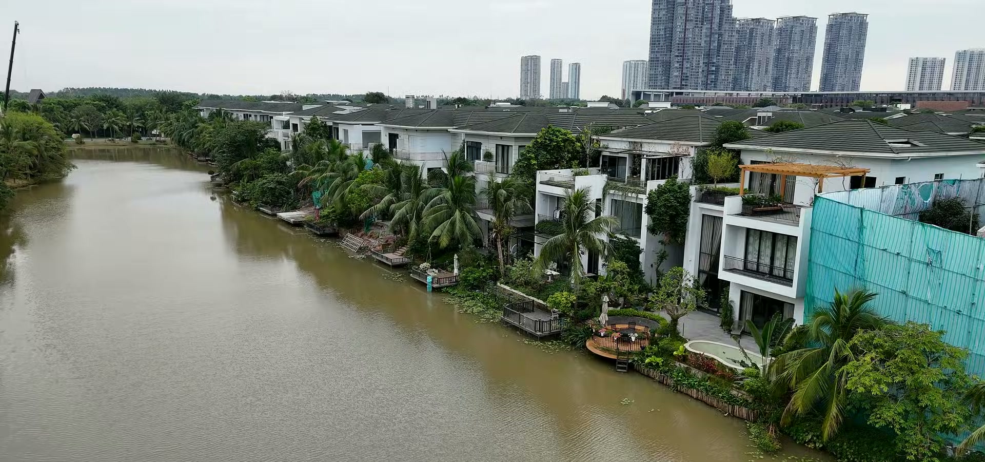 Dãy biệt thự đảo Ecopark nhìn từ trên mặt nước, sân sau từng căn có decking gỗ, dàn pergola, cây dừa và bể bơi nhỏ chạy sát mép nước