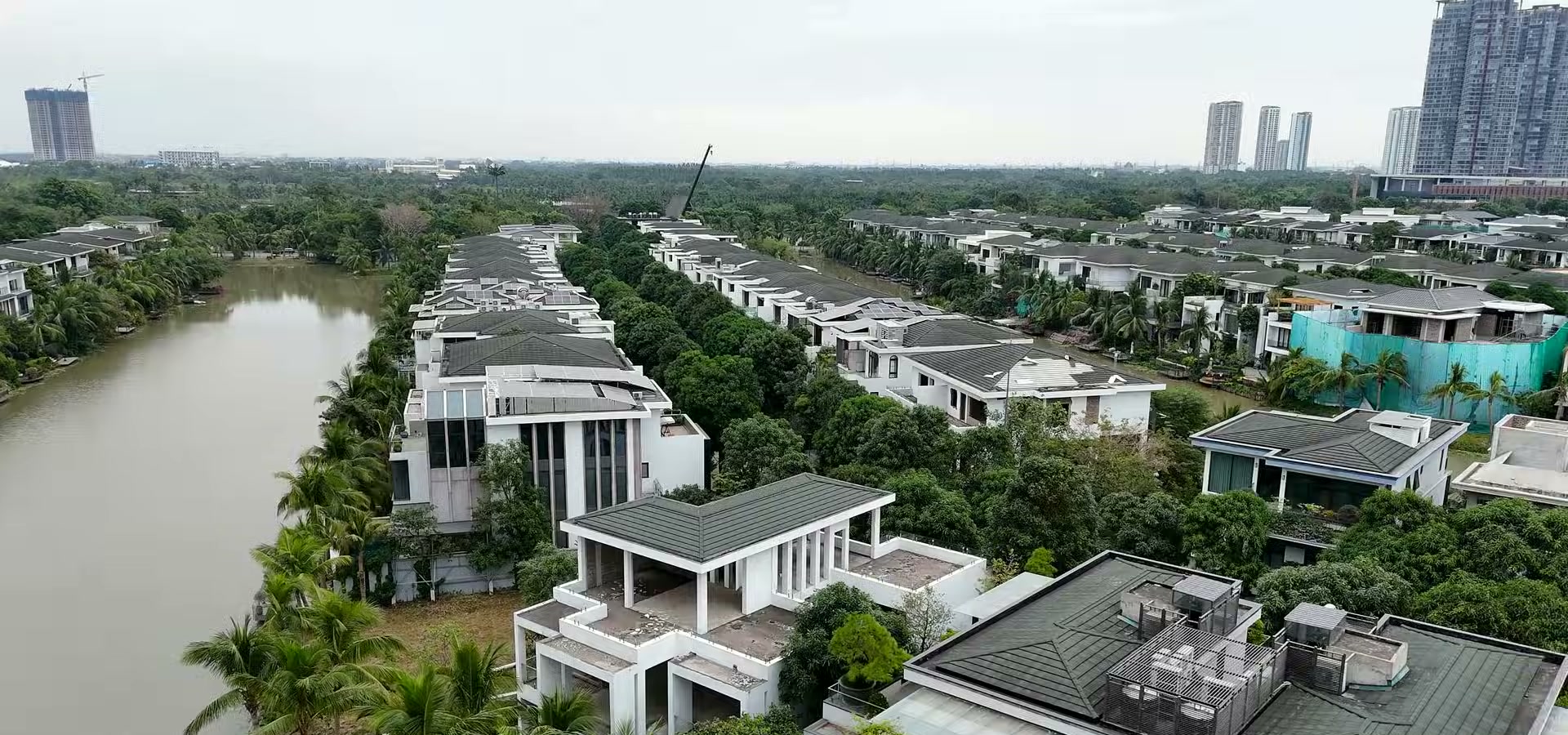 Nhìn từ trên cao xuống khu biệt thự đảo Ecopark, hai dãy nhà mái sẫm nằm hai bên một nhánh nước, phía xa là các toà cao tầng và một căn đang hoàn thiện phần thô